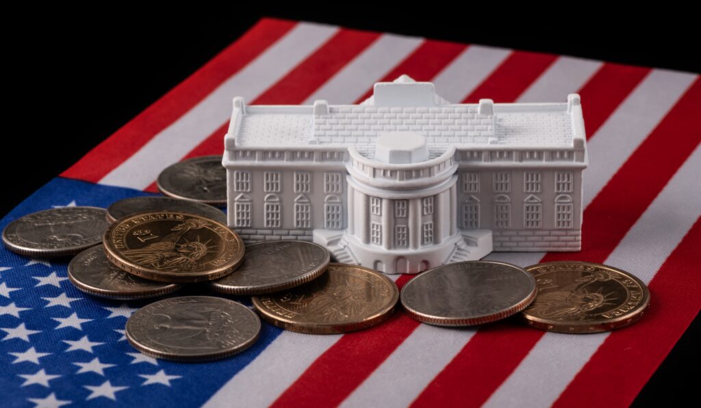 A miniature White House model on top of an American flag, surrounded by coins